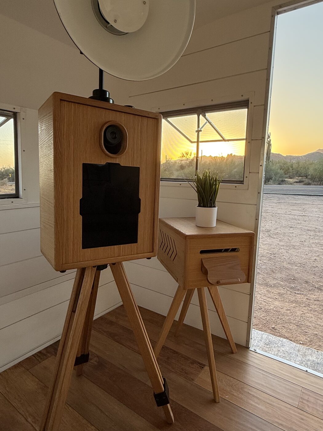 Inside the trailer studio — the wooden booth and print stand bathed in sunset light