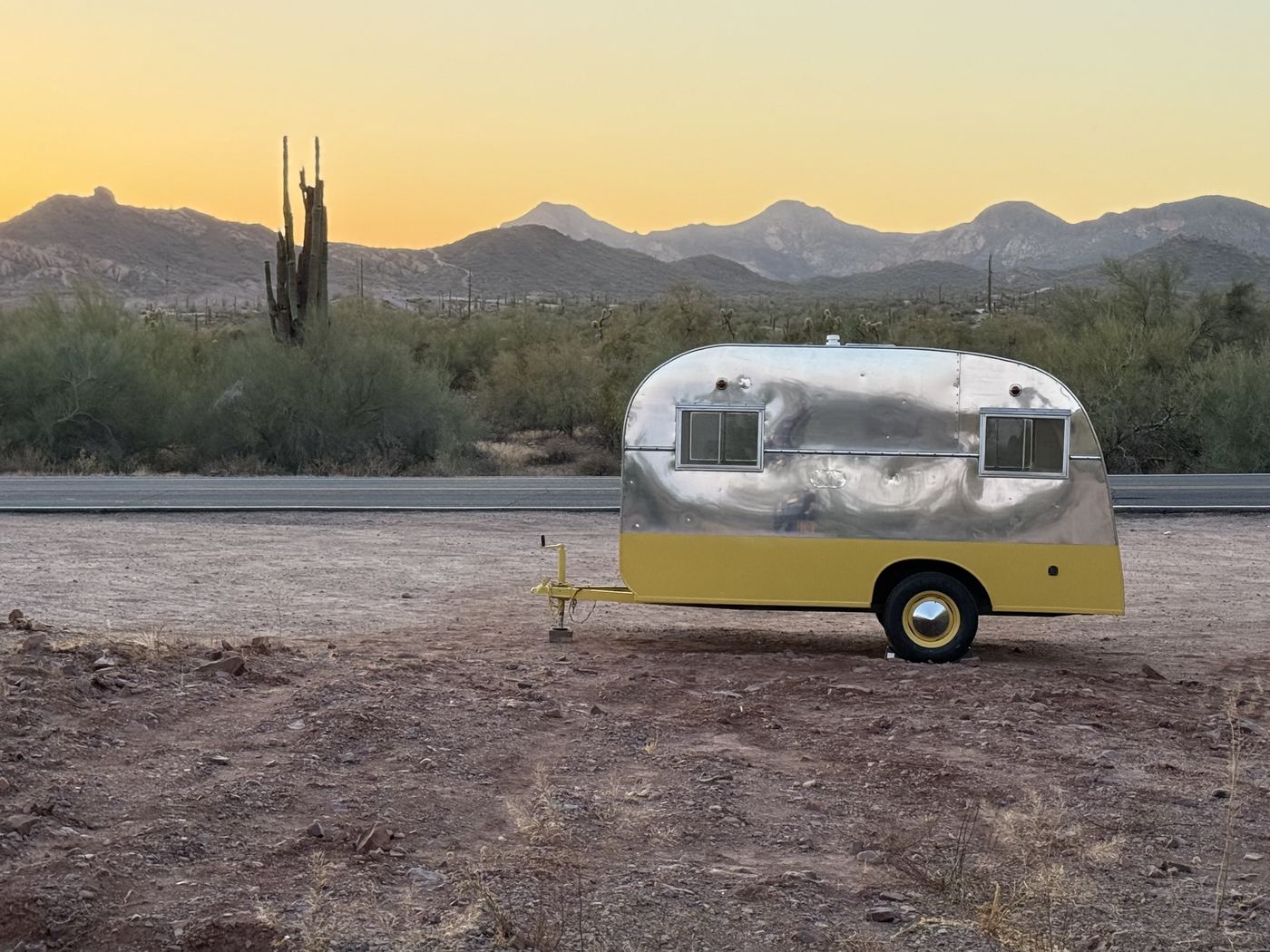 The chrome trailer parked beneath a wide Arizona sunset with saguaros and mountains
